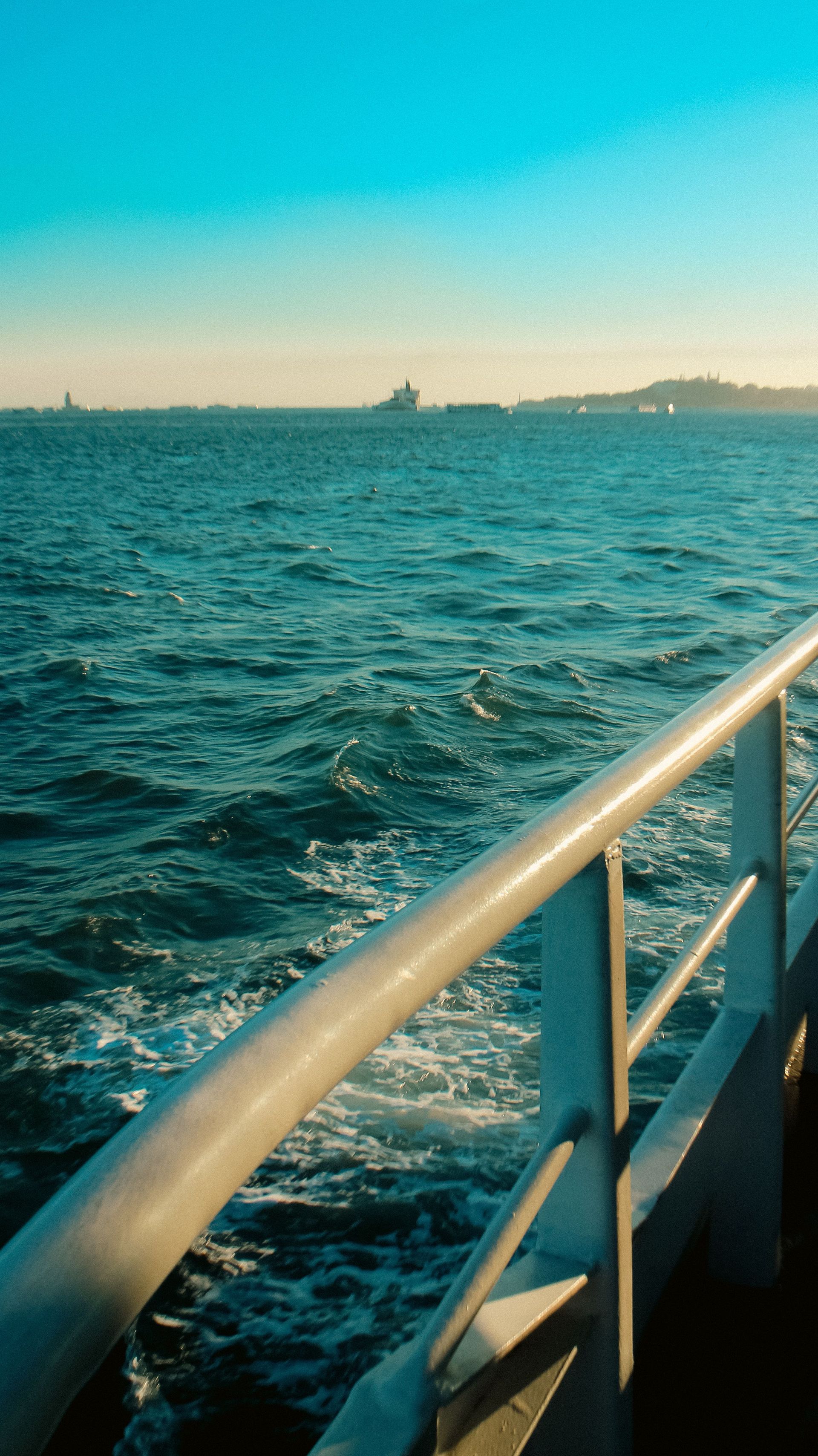 A peaceful ocean scene captured from a ship's deck with distant coastlines and clear blue skies.